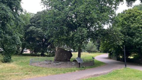 A large rock under the shade of a big gree tree.