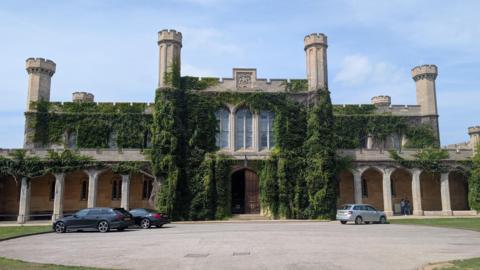 An exterior shot of Lincoln Crown Court. Three cars are parked in front. The sky is blue.