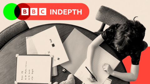 Two children sit around a circular table with textbooks, paper, a clock and a teddy bear