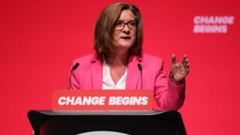 Eluned Morgan speaking at a Labour conference in front of a red background.