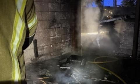 A burned looking shed with fire water hoses in the frame 