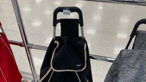 A black shopping trolley, next to a railing inside a supermarket, with a paper ticket number taped to it