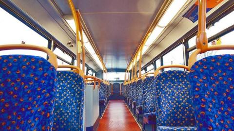 A bus, with a large number of blue and red seats, with a red aisle in the middle. There are yellow handles on the back of the seats and yellow poles. 