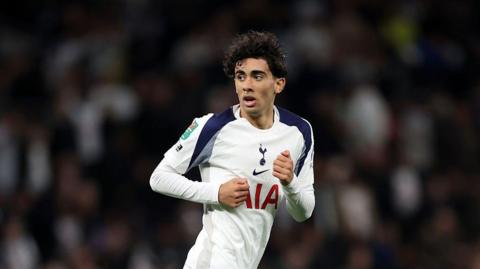 Luca Williams-Barnett is dressed in a Spurs strip and is running across a pitch. He has short, dark curly hair and is looking to the side.