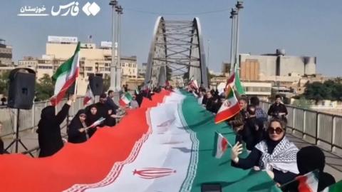 People stand on either side of the Iranian flag on the White Bridge in Ahvaz, Iran