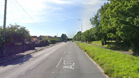 a dual carriageway with housing and grass verge, cars driving further up the road