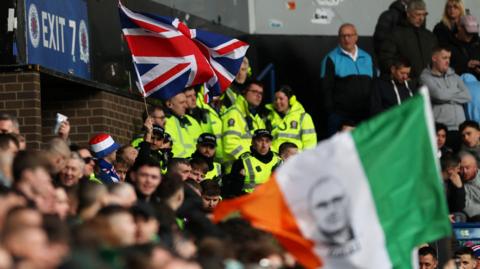 Police officers inside the stadium between flag waving Rangers and Celtic fans before a Scottish Cup match at Ibrox