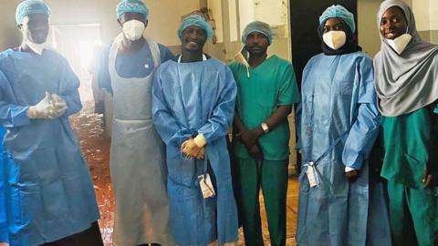 A group of medics at Saudi Hospital in el-Fasher in scrubs smile as they stand for a group photo after successfully performing two-hour emergency caesarean under bombardment. Dust from the shell damage can be seen on the floor