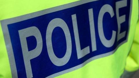 A close up of a police officer's high visibility jacket. The word "police" is in silver letters on a dark blue background.