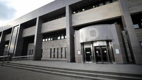 The exterior of Glasgow Sheriff Court, a grey building with a rotating door entrance