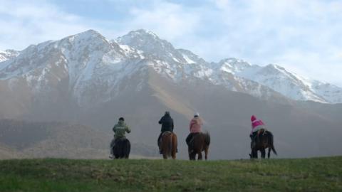 Four people riding away from the camera on horseback with mountains in the distance.