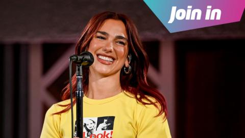 Dua Lipa stands in front of a microphone wearing a yellow t-shirt.