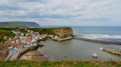 An aerial view of the village of Staithes which shows the pier stretching out into the sea to the right of the image. 