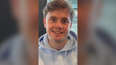 Jack wearing a grey hoodie smiling into camera