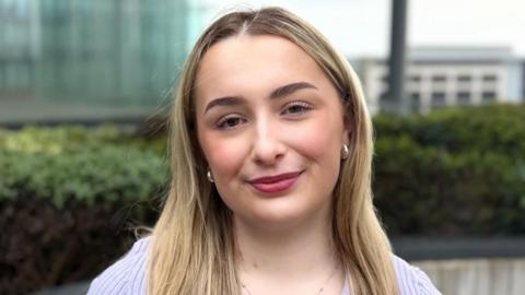 Layla has long blonde hair past her shoulders and is wearing silver earings.