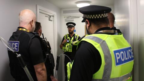 Five uniformed police officers gathered in a communal area of the block of flats. 