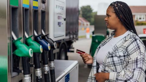 Woman filling her car at a petrol station, holding a credit card