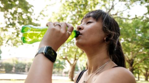 Woman in park drinks from green bottle 