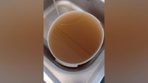 Brown water in white bowl on silver sink