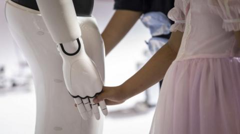 A child holds the hand of a robot at an AI conference in Shanghai, China, on 7 July 2023