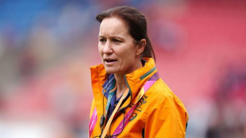 A woman with tied back brown hair is pictured wearing a yellow Australian team jacket. 