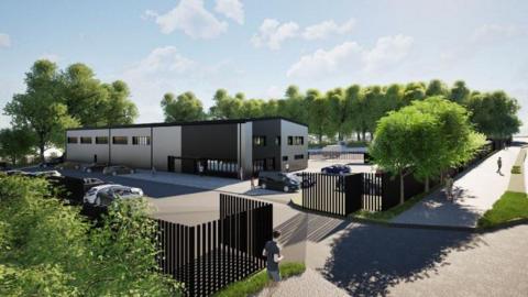 Artist's impression of waste vehicle depot planned for East-the-Water in Devon. The design has a row of grey and black buildings with large black fencing around the site and trees dotted along the edge.