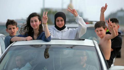 Children gesture as they hang out of a car as Lebanese people return home