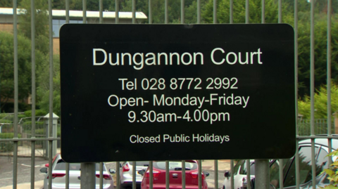Shows a black and white sign for Dungannon court attached to an iron gate