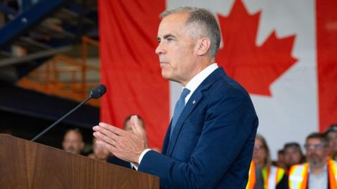Mark Carney making a speech in front of a lectern with a large Canadian flag in the background