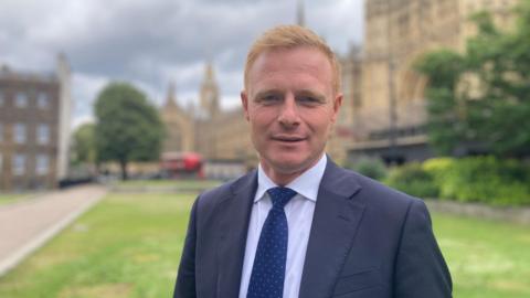 Robbie Moore MP wearing suit outside Parliament