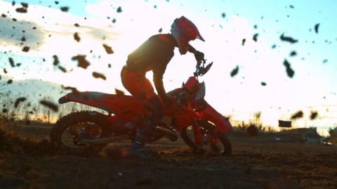 A motorbike rider turns a sharp corner, spraying chunks of mud in the air. 