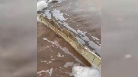 Sharp-ish white plank sticking out of sand with water flowing over it