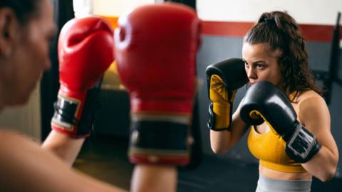 A young female kickboxer sparring with a female coach, during kickbox practice in the gym