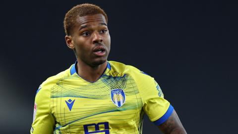 Owura Edwards in action for Colchester United. He is wearing a yellow and blue away shirt.