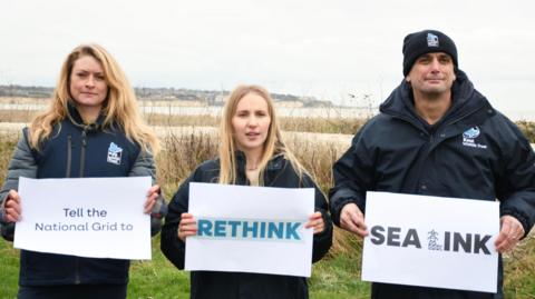 campaigners holding signs which say "tell the National grid to rethink sea link"