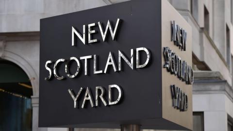 A 3D triangular sign which says 'New Scotland Yard' on both visible sides. 