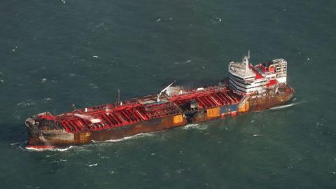 Aerial view of the Stena Immaculate with red decks and white superstructure with a hole in its hull and burn marks around the side of the ship