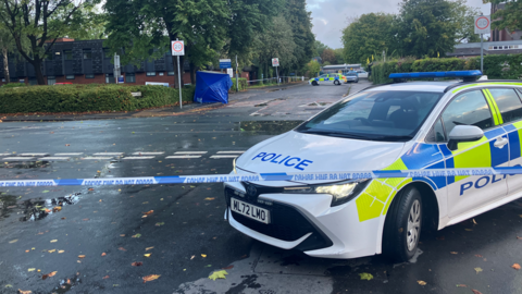 The scene of the stabbing with a police car in the foreground and a blue forensic tent in the background