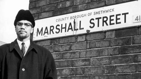 Malcolm X stands by a street sign for Marshall Street in Smethwick.