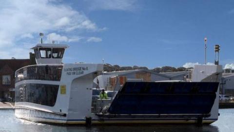 The Floating Bridge 6 crossing the River Medina. It is white, with large blacked out glass panelling and a ramp 