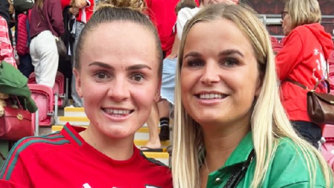 Lily Woodham - wearing a Wales shirt - with a friend at a game. They are both smiling at the camera