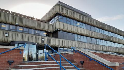 Outside of Lincolnshire Police headquarters a grey concrete and glass three-storey building with brick steps up to the main entrance