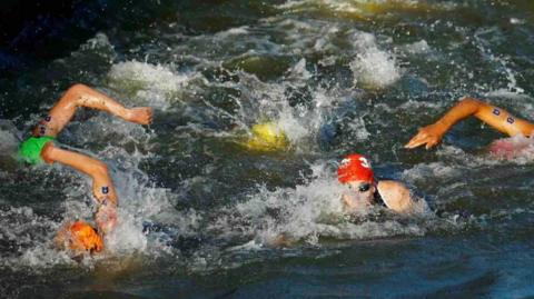 Five triathlon swimmers front crawling while wearing brightly coloured swim caps