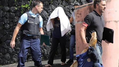 French police escort a person who is hidden under a towel