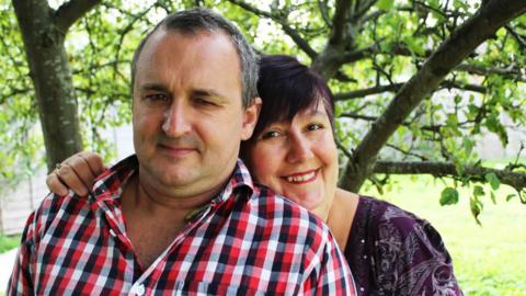 Michael Ramstedt wearing a checked shirt with a woman hugging him