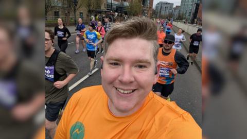 Scott Storey, a man in his late 30s, smiling whilst running alongside other participants in the Sheffield Half Marathon.