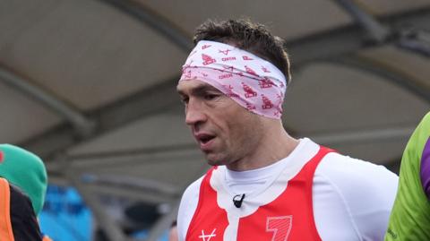 Kevin Sinfield on his charity fundraising run, he is wearing a red and white running vest and a white headband