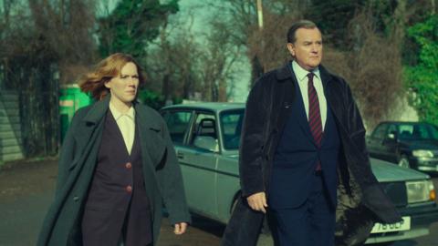  Nicki Jennings (CHARLOTTE SPENCER), Brian Boyce (HUGH BONNEVILLE) walking in front of a car.