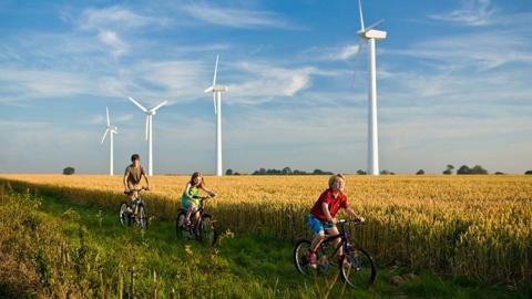 Kids cycling past wind turbines in the country