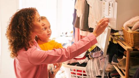 A woman holding a small child is checking her boiler at home 